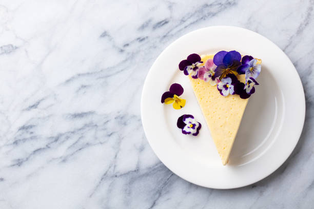 Cheesecake decorated with edible flowers on white plate. Marble background. Cheesecake decorated with edible flowers on white plate. Marble background. Copy space. Top view. edible flower stock pictures, royalty-free photos & images