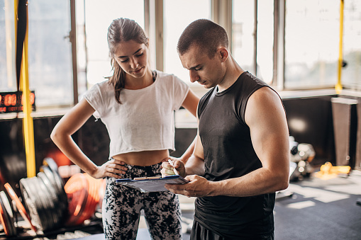 Young fit woman making fitness plan with her personal trainer in the gym.