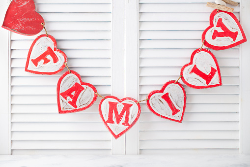 Wooden decorative letters family sign, garland on white blinds background. Copy space.