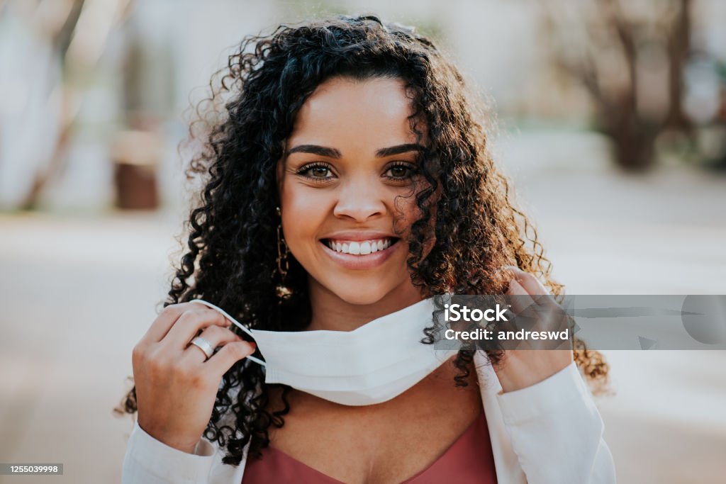 Woman smiling while taking face protection mask Woman afro during pandemic isolation at city. Removing mask from face. Protective Face Mask Stock Photo