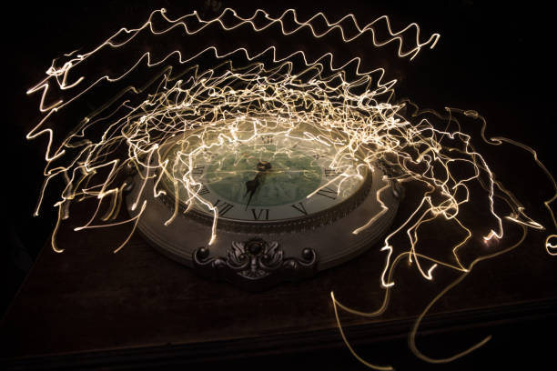 istock Time concept. Big vintage round clock on wooden table with abstract light. 1255040162