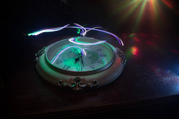 istock Time concept. Big vintage round clock on wooden table with abstract light. 1255040163