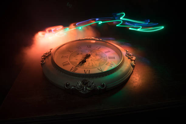 istock Time concept. Big vintage round clock on wooden table with abstract light. 1255040170