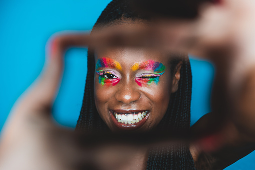 Woman looking straight to camera with a rainbow colored makeup on eyes. Studio shot.