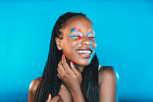 Woman looking straight to camera with a rainbow colored makeup on eyes. Studio shot.