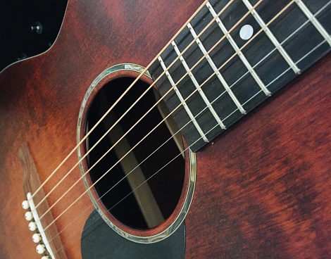 Against a backdrop of rich, dark wood, a single guitar commands attention. The close-up shot highlights every grain and texture of the instrument's body, drawing the viewer into its warm, inviting embrace. With its strings delicately poised and its frets ready to be explored, the guitar exudes a sense of timeless beauty and craftsmanship.
