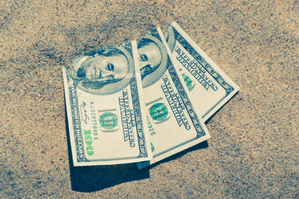 istock Money dolars half covered with sand lie on beach close-up. 1255049252
