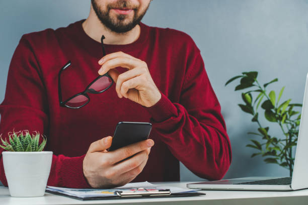 istock Cropped shot of casually dressed bearded man reading message on his mobile phone while sitting at white office desk 1255053132