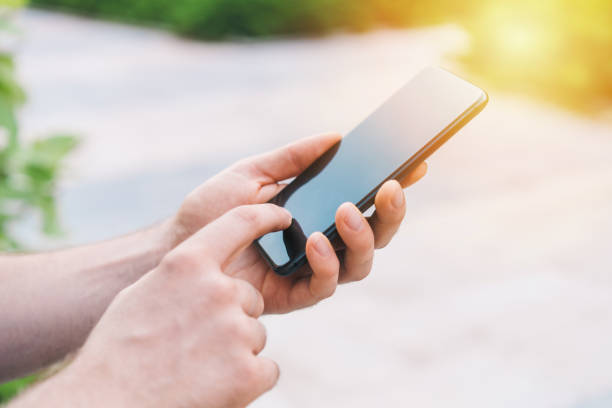 istock Close up crooped shot of man hands holding smartphone and touching it's sensor screen browsing mobile application outdoors 1255054453