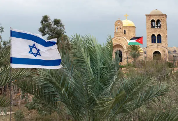 Church of St. John the Baptist on the Jordan River with the flag of Jordan and the flag of Israel in front, on the border of these countries. Baptismal Site of Jesus Christ  in the Galilee is a sacred place for all Catholics and Orthodox Christians on the Holy Land.