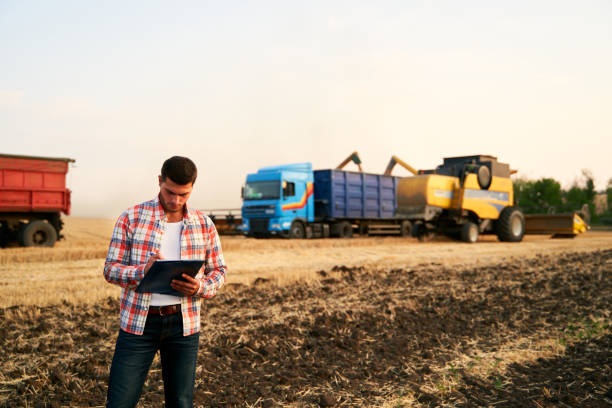 istock Farmer controls loading wheat from harvester to grain truck. Driver holding clipboard, keeping notes, cargo counting. Forwarder fills in consignment waybills. Agricultural commodities logistics 1255055102