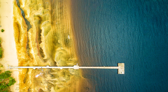 Long jetty with magical sandy pattern that´s fades into water, aerial view