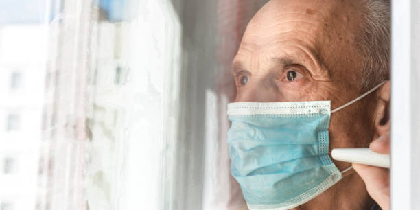 istock old man in blue disposable face mask looks through window 1255058491