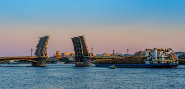 General cargo ship with raw wood logs on deck underway on Neva river at summer sunrise.