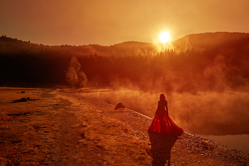 High angle view of woman walking on the edge of water at the lake at sunset time, wearing red skirt