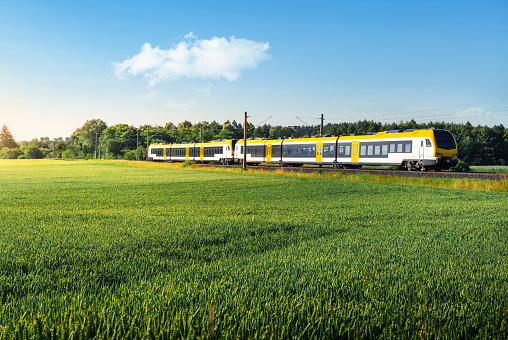 Electric passenger train traveling through agricultural fields, at sunrise, in Schwabisch Hall, Germany. Eco-friendly German yellow commuter train.