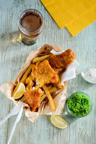 istock Deep fried fish and chips in combination with lemon slices, green peas and beer 1255076586