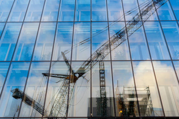 odbicia frane i placu budowy w szklanej elewacji biurowca. - blue construction construction site crane zdjęcia i obrazy z banku zdjęć