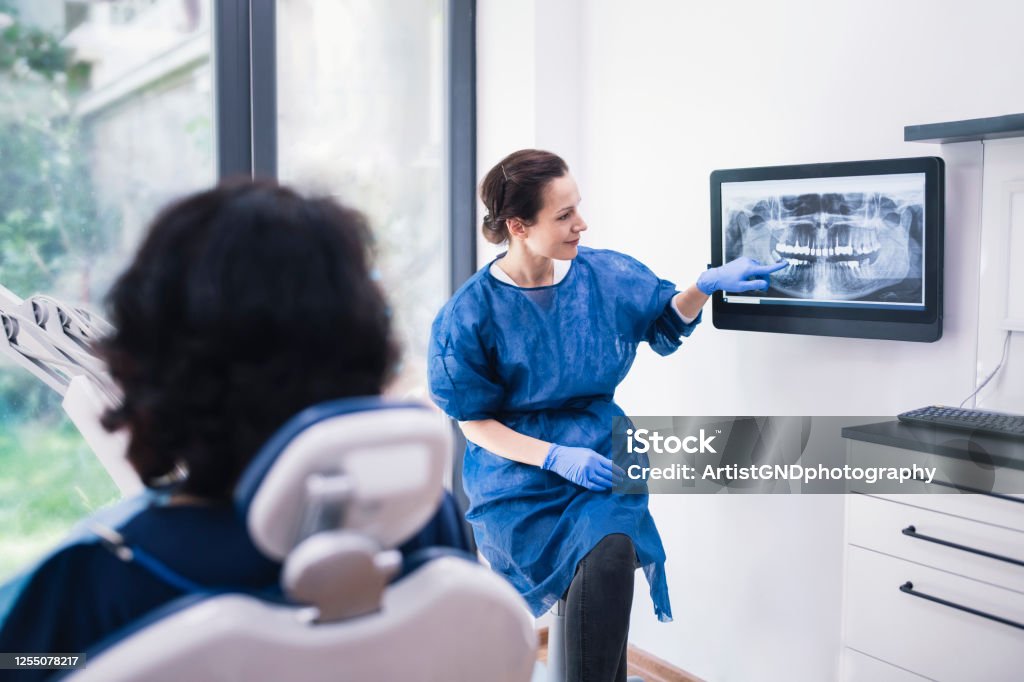 Dentist Explaining Tooth X-Rays To A Patient. Female dentist explaining tooth x-rays to a unrecognizable patient. Dentist Stock Photo