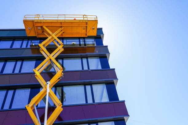modern building facade repair using a high scissor lift with a platform modern building facade repair using a high yellow scissor lift with a platform cladding construction equipment photos stock pictures, royalty-free photos & images