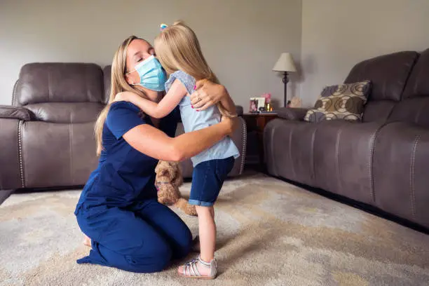 A 3 year-old girl hugs her Mommy after helping her put on a face mask before she leaves for work as a nurse, Indiana, USA