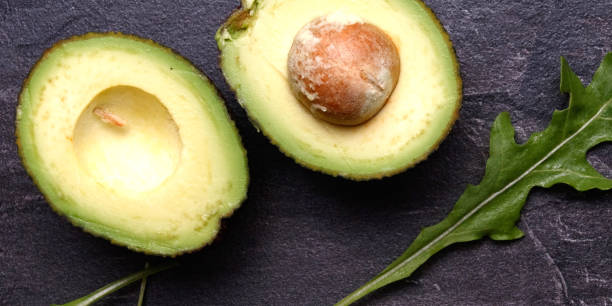 istock Two halves of avocado, one with a bone on a dark background. 1255092462