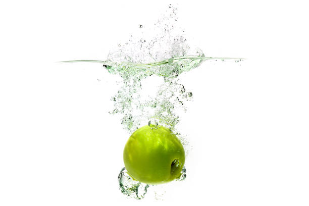 one green apple falling into water on a white background with splashes, drops and bubbles - wet apple imagens e fotografias de stock