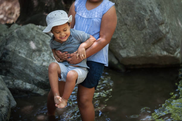Big sister holding her little brother above the cold water from a pond while he is nervous. stock photo