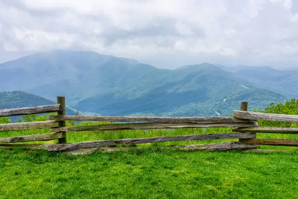Photo of Devil's Knob Overlook green grass field meadow and fence at Wintergreen resort town village near Blue Ridge parkway mountains in summer clouds mist fog covering rolling hills