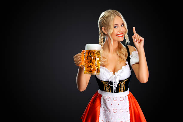 Smiling young sexy Beer Fest girl waitress, wearing a traditional Bavarian or german dirndl, serving big beer mug with drink isolated on black background. stock photo