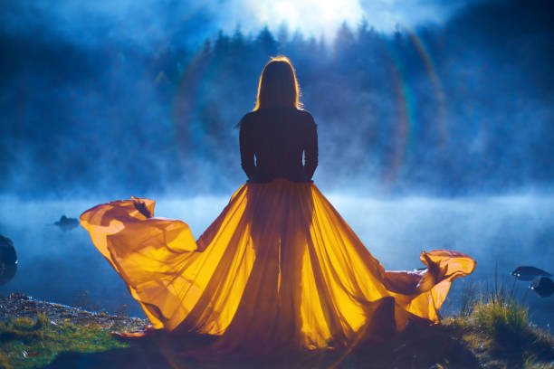 Rear view of woman wearing yellow skirt posing at the lake on the edge of water looking at view