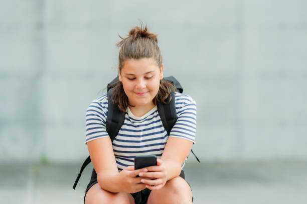 istock A smiling thirteen year old student is seating on a pic nic table in front of her school while writing message SMS. 1255117869