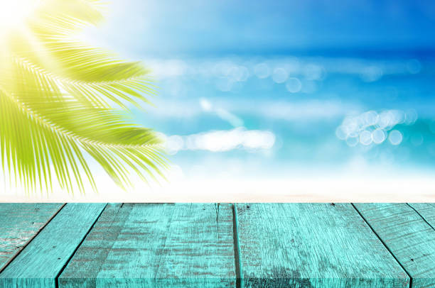 istock Blur tropical beach with bokeh sun light wave and palm tree on copy space empty old wood table abstract background. 1255120869