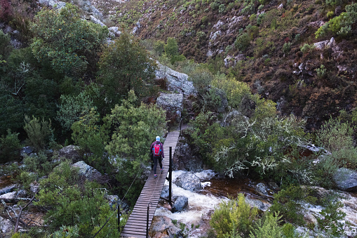 A woman walks across a swing bridge as she hikes in the mountains. Woman enjoying the outdoors and nature