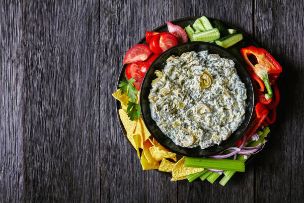 Spinach Artichoke cheese Dip set with Tortilla Chips, cucumber, celery sticks, tomato slices and red bell pepper, Spinach Artichoke leafy cheese Dip in a bowl with Tortilla Chips, cucumber, celery sticks, tomato slices and red bell pepper, horizontal view from above, flat lay, free space dipping photos stock pictures, royalty-free photos & images