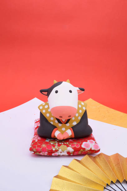 A clay sculpture of a cow masquerading as a traditional Japanese character, Fukusuke. Handmade clay doll. On red and white background. Vertical position. zabuton stock pictures, royalty-free photos & images