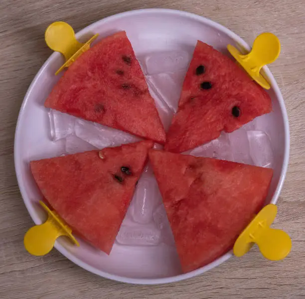 Photo of Watermelon slices in a bowl with ice on an ice cream stick on a wooden background. Creative idea