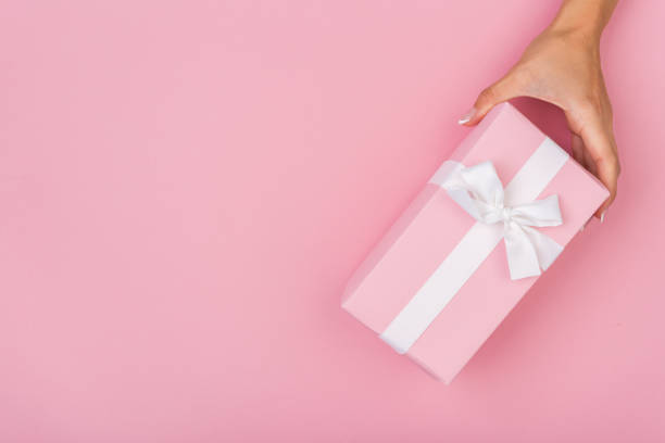 istock Top view of female hands holding present box package in palms, on pink background 1255142865