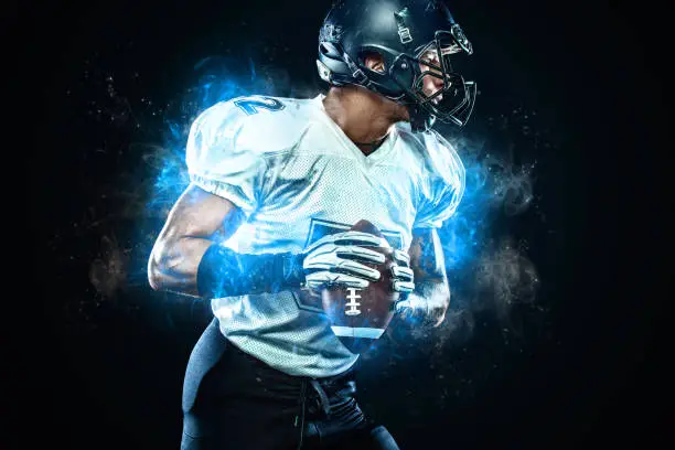 Photo of American football player in helmet with ball in hands. Fire background. Team sports. Sport wallpaper.