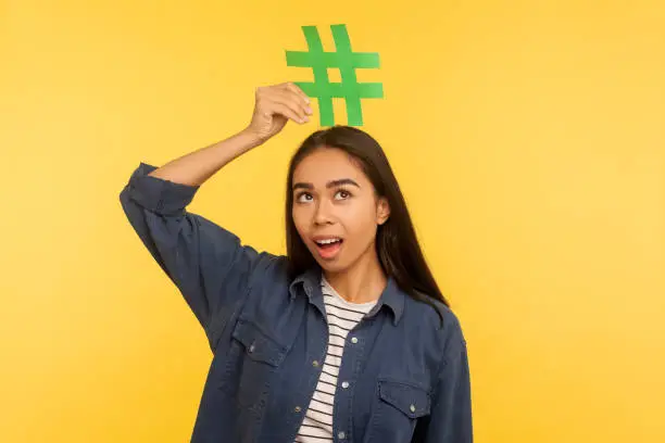 Photo of Viral topic, popular internet idea. Portrait of thoughtful surprised girl holding hashtag symbol on head