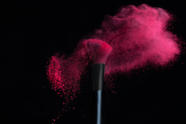 Brosse de maquillage avec l’explosion rose de poudre isolée dans un fond noir - Photo