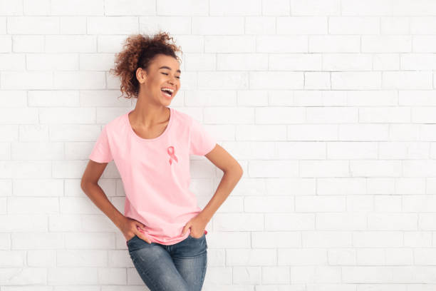 Woman Wearing Pink T-Shirt With Ribbon Symbol Over White Wall Breast Cancer. African American Woman Wearing Pink T-Shirt With Ribbon Symbol Posing Over White Wall. Free Space breast photos stock pictures, royalty-free photos & images