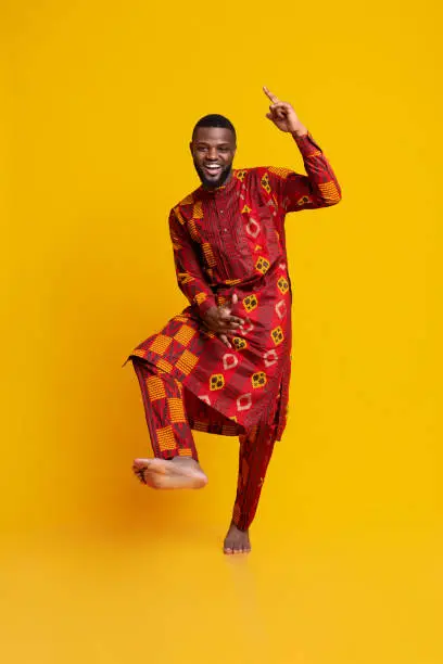 Cheery black guy in authentic dress having fun over yellow background