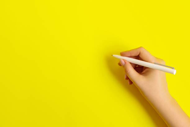 istock Female hand with a white pen on a yellow background. 1255153944
