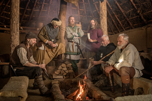 A family group of viking male villagers having a fun meeting in a warm settlement hall