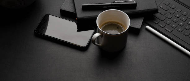 istock Dark modern workspace with tablet keyboard, smartphone, coffee cup, schedule books and copy space 1255165945