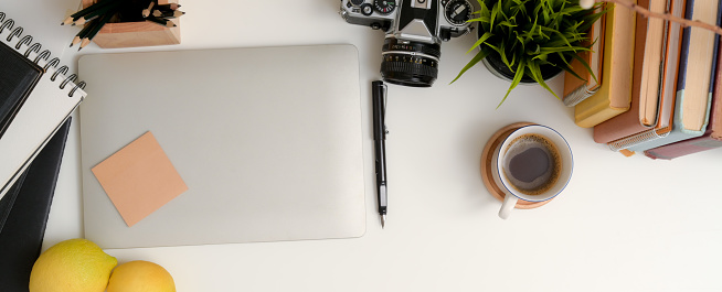 Top view of modern workspace with laptop, stationery, camera, books and decorations on white table