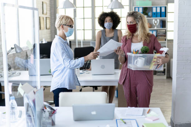 Manager dismissing a  colleague due to coronavirus job crisis Female business manager dismissing a colleague due to limiting of work places during Coronavirus pandemic office cubicle mask stock pictures, royalty-free photos & images