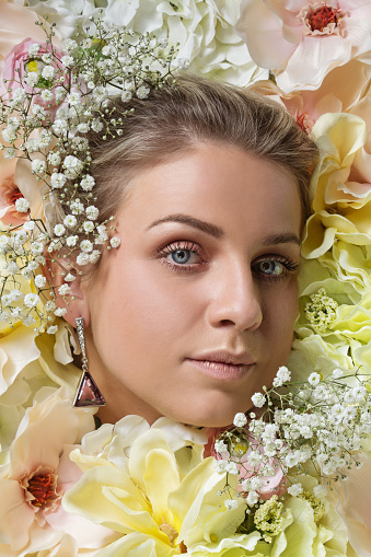 A beautiful woman's female face laying in a colourful bed of pastel white roses and other flowers
