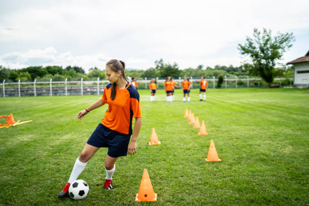 Female soccer player practicing Young female soccer player training on a football field. Young woman practicing her skills, football team standing behind. high school soccer stock pictures, royalty-free photos & images